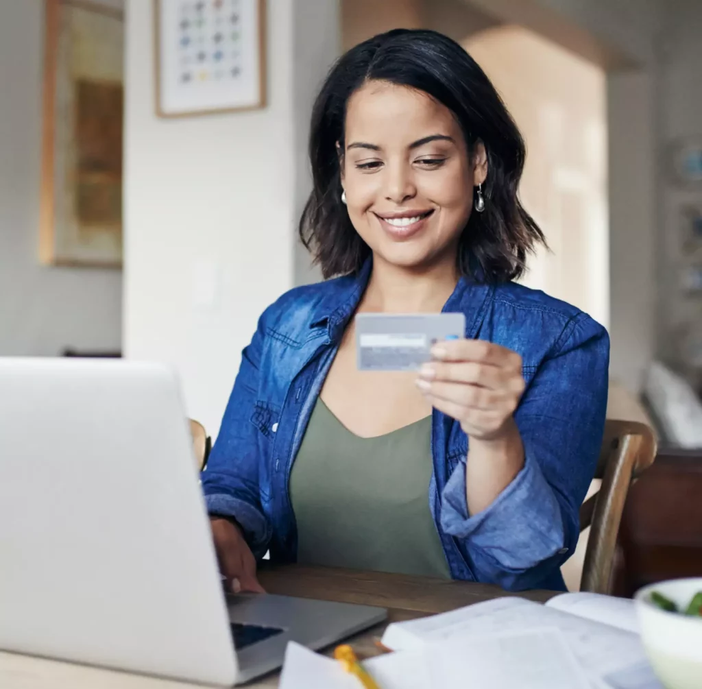 Smiling woman making an online payment with a credit card while using her laptop at home.
